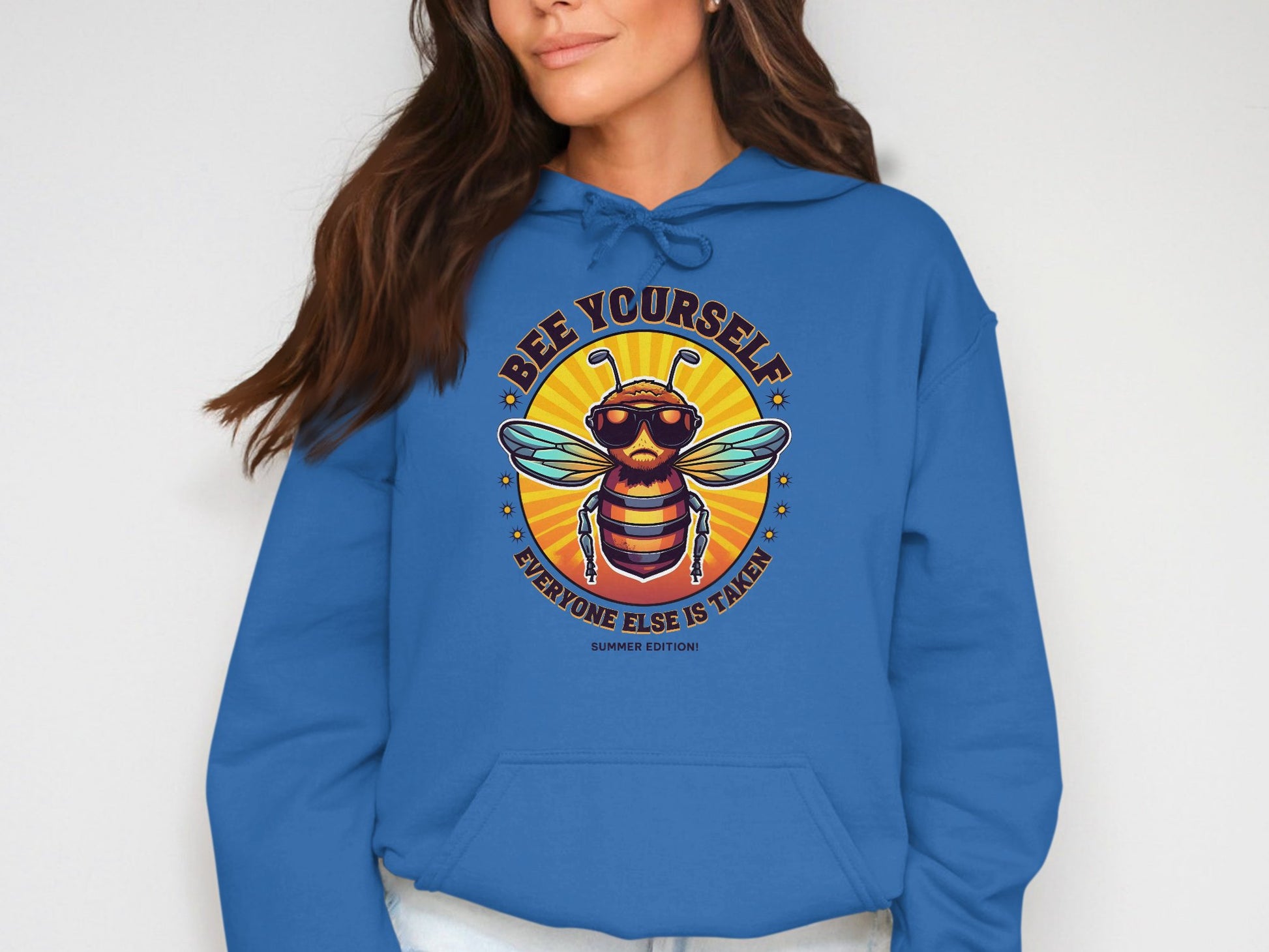 Someone is wearing Garment Graphics Summer Edition Hoodie, featuring a cartoon bee with sunglasses on a blue backdrop. Above it, the slogan reads BEE YOURSELF and below EVERYONE ELSE IS TAKEN, set against a vibrant yellow-orange gradient circle.