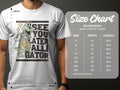 A casually dressed person wears a white Garment Graphics T-shirt featuring a cartoon alligator with a basketball and the See You Later Alligator slogan. Nearby, theres a size chart for Gildan 5000 heavy cotton T-shirts showing sizes and dimensions in inches.