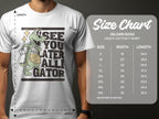A casually dressed person wears a white Garment Graphics T-shirt featuring a cartoon alligator with a basketball and the See You Later Alligator slogan. Nearby, theres a size chart for Gildan 5000 heavy cotton T-shirts showing sizes and dimensions in inches.