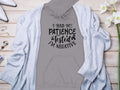 A Garment Graphics gray hoodie stating I had my patience tested, Im negative is matched with a light blue cardigan on wood, accompanied by white shoes, jewelry, glasses, and white flowers for a chic and casual ensemble.