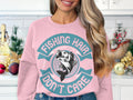 In a festive kitchen with holiday decorations and a white tiled backsplash, a fishing enthusiast wears Garment Graphics light pink sweatshirt, featuring a fish graphic and the phrase Fishing Hair Dont Care.