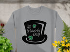 A Garment Graphics stylish gray sweatshirt features a black top hat graphic with St Patricks Day and two green shamrocks. It captures the festive spirit, surrounded by small plants and flowers on a light gray surface.