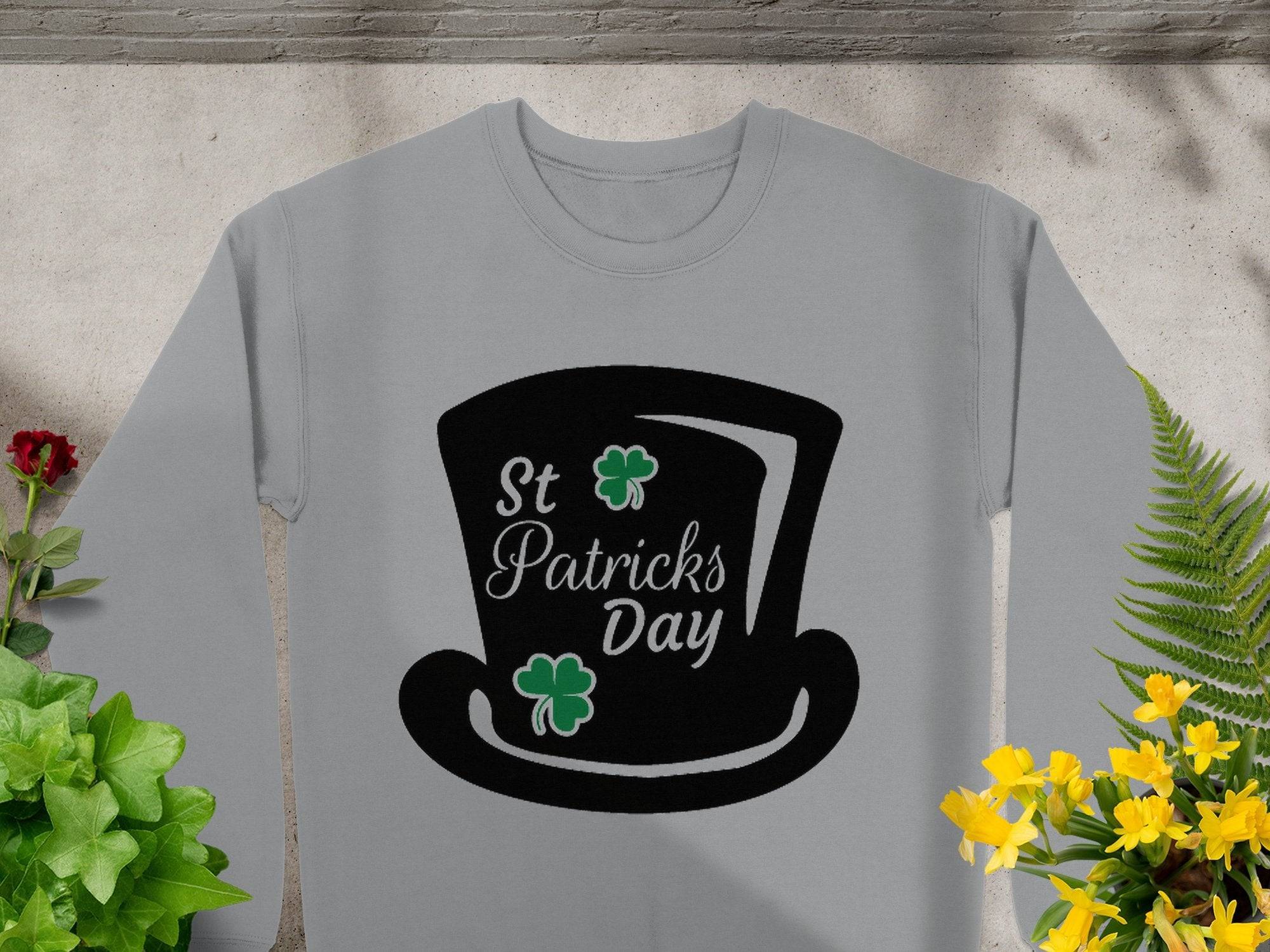 A Garment Graphics stylish gray sweatshirt features a black top hat graphic with St Patricks Day and two green shamrocks. It captures the festive spirit, surrounded by small plants and flowers on a light gray surface.