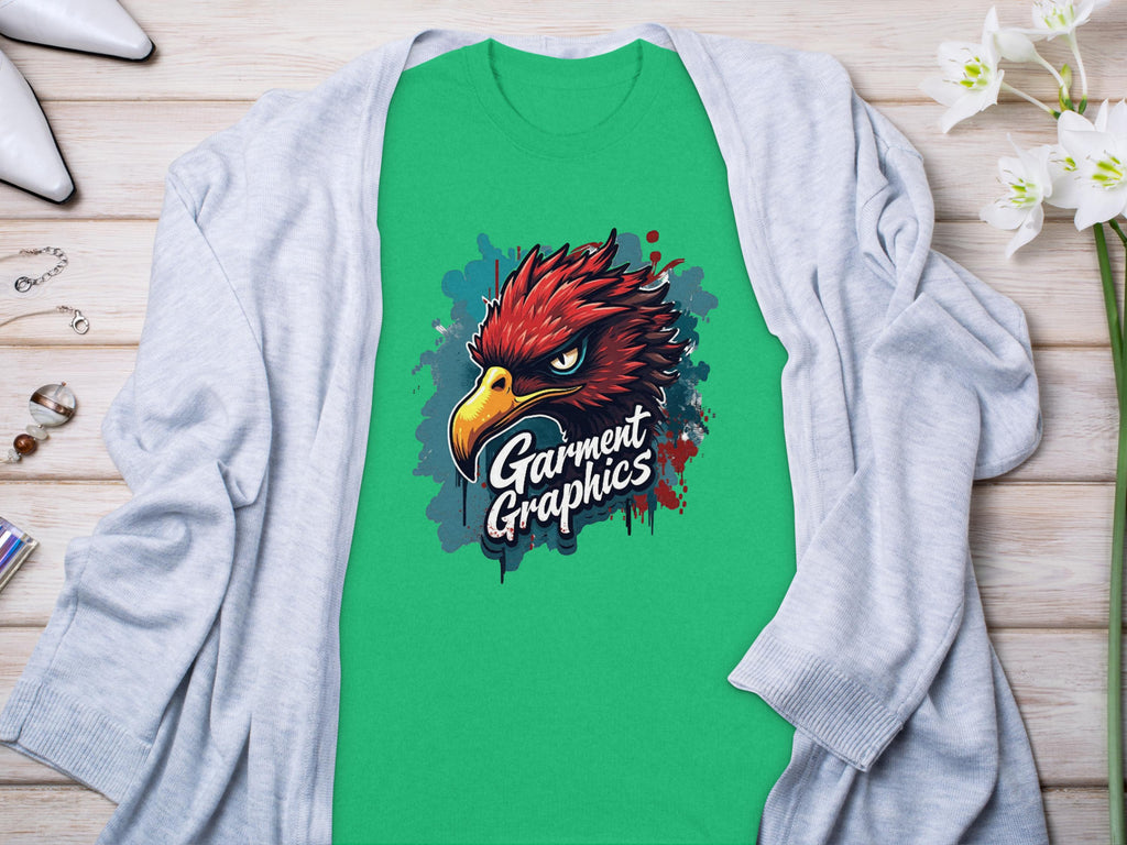 A green Garment Graphics t-shirt with an Eagle design lies on a light wooden surface. Its artfully draped with a gray cardigan and accessorized with white high heels, jewelry, and flowers nearby.