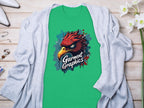 A green Garment Graphics t-shirt with an Eagle design lies on a light wooden surface. Its artfully draped with a gray cardigan and accessorized with white high heels, jewelry, and flowers nearby.