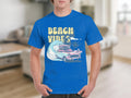 Someone wearing a Garment Graphics blue t-shirt with a Beach Vibe design that includes a classic car, surfboards, palm trees, and ocean waves. The setting is an indoor living room.