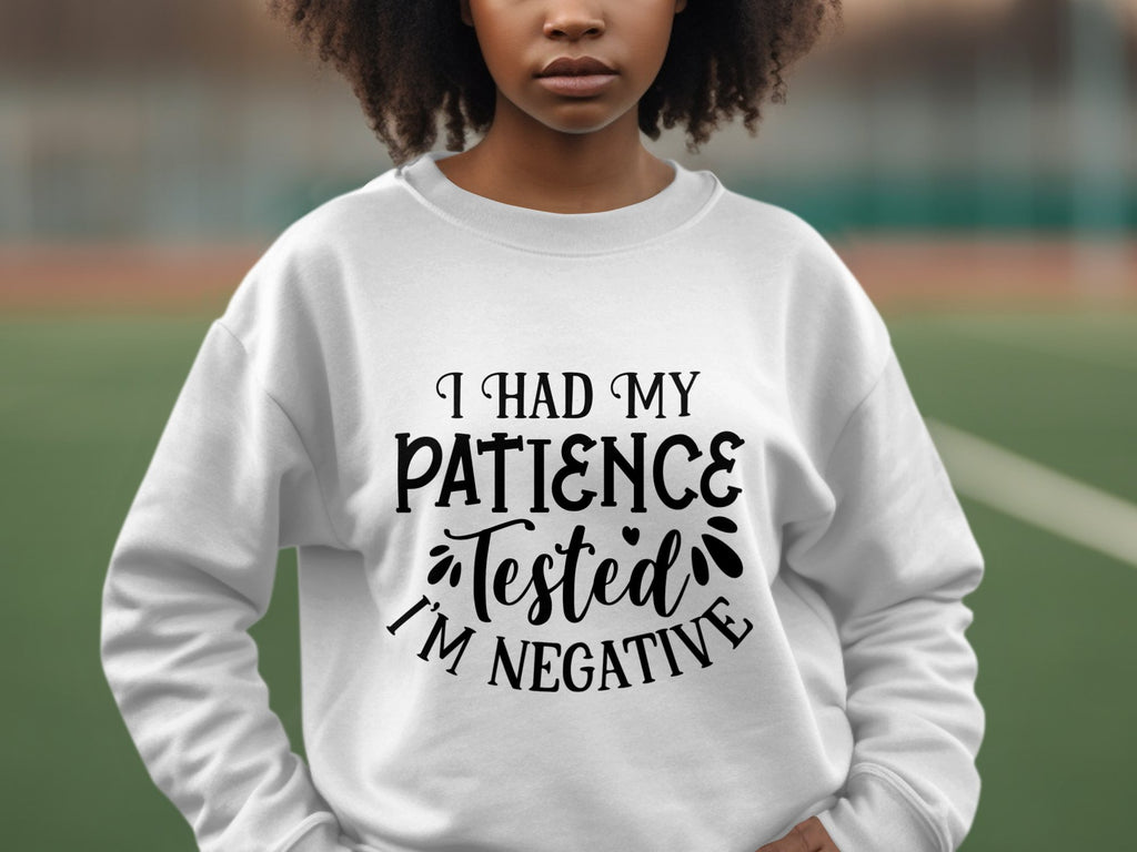 A person outdoors wears a quirky Garment Graphics sweatshirt with I had my patience tested, Im negative text. The unisex sizing suits casual outings, while a softly blurred sports field in the background adds to the relaxed atmosphere.