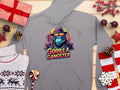 A Garment Graphics gray streetwear hoodie with a Gorilla Gangster design, showing a cartoon gorilla in a hat and sunglasses, is on a wooden surface amidst Christmas decorations including gift boxes, pinecones, and a cozy sweater.