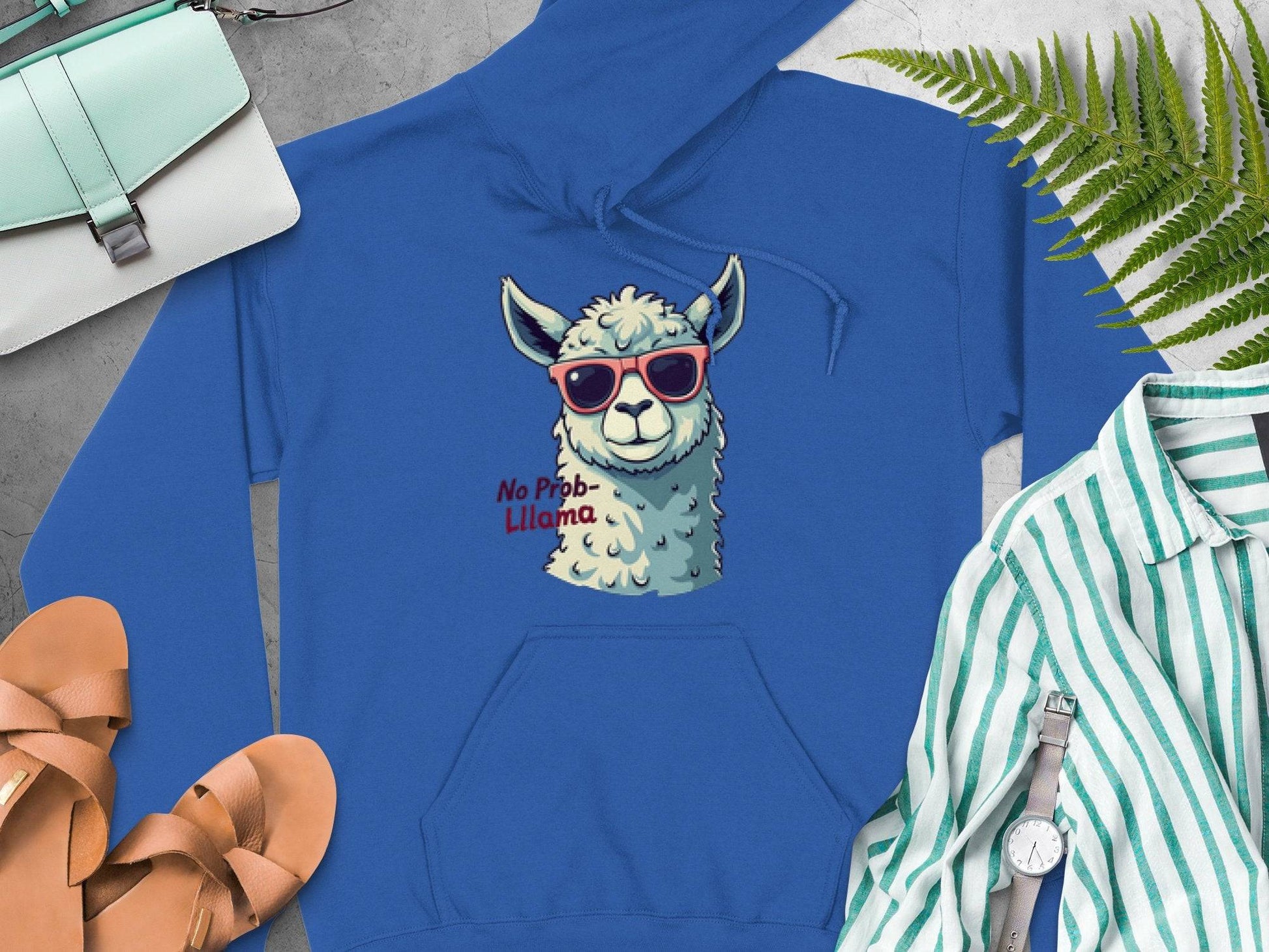 The Garment Graphics blue hoodie features a llama with funny sunglasses and the words No Prob-Llama, surrounded by a turquoise handbag, brown sandals, a striped shirt, a wristwatch, and a fern leaf. This classic fit hoodie adds humor to your wardrobe.