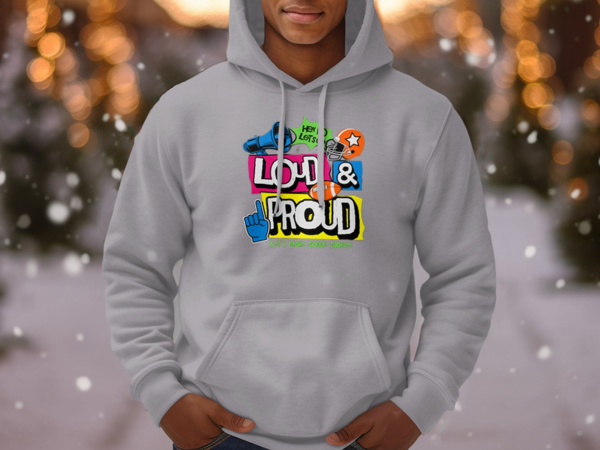 A person in a gray hoodie with vibrant graphics from Garment Graphics confidently displays LOUD & PROUD. The softly blurred backdrop adorned with twinkling lights and snow captures the essence of the Lets Make Some Noise vibe perfectly.