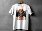 Garment Graphics presents the Bullocks Pintable T-Shirt, a classic fit white tee on a wooden hanger against a gray wall. It features a bulls head illustration with large horns and BULLOCKS in bold orange letters, framed by an orange circle, making it perfect for family sizing.