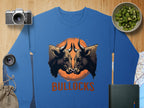 Garment Graphics blue sweatshirt showcases a striking bullocks print with two bulls facing an orange circle and BULLOCKS below. It is displayed among a camera, lens, cucumbers in a bowl, map, book, and small bag on a wooden surface.