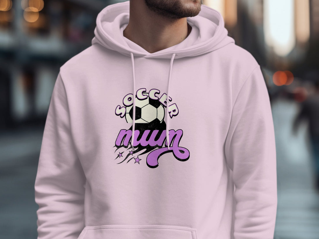 A person stands wearing a cozy black hoodie from Garment Graphics, featuring Soccer Mum in white and purple with a soccer ball graphic and star accents. This classic fit hoodie is perfect for those who embrace their sporty spirit with style.