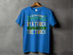 Garment Graphics blue T-shirt humorously highlights English politeness with the text If an Englishman gets run down by a truck, he apologizes to the truck in vibrant white, yellow, green, and blue fonts on a gray background.