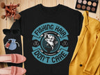 The Garment Graphics black shirt features a circular fish logo and the text, Fishing Hair Dont Care. Its stylishly paired with a mustard jacket, makeup palette, sunglasses, red shoes, brushes, and a pouch on a wooden surface—ideal for fishing enthusiasts.