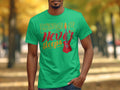 Outdoors, a person wears a Garment Graphics T-shirt made of green 100% cotton, featuring Music Never Sleeps and an electric guitar graphic in colorful letters. Blurred autumn trees in the background beautifully complement the vibrant shirt design.