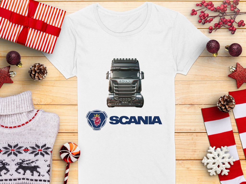 Celebrate the season with Garment Graphics Scania T-shirt. This white tee boasts a Scania truck graphic and logo, accented by festive decor such as wrapped gifts, pinecones, red stars, a cozy sweater, and candy canes on a wooden surface—ideal for automotive enthusiasts.