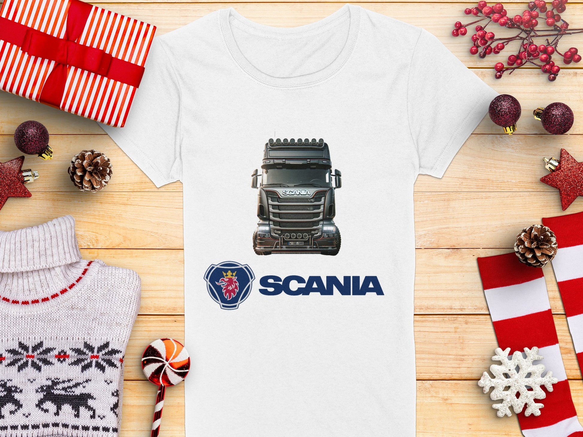 Celebrate the season with Garment Graphics Scania T-shirt. This white tee boasts a Scania truck graphic and logo, accented by festive decor such as wrapped gifts, pinecones, red stars, a cozy sweater, and candy canes on a wooden surface—ideal for automotive enthusiasts.