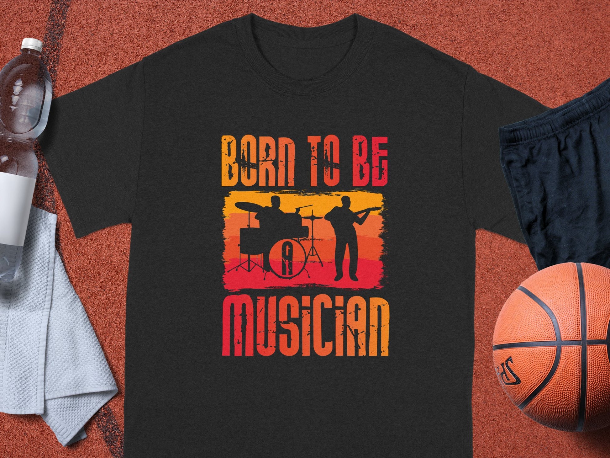 The Garment Graphics black t-shirt showcases a vibrant graphic of a drummer and guitarist with red and yellow stripes, declaring Born to Be Musician. Its ideal for music lovers and is displayed on an orange surface with a basketball, shorts, water bottle, and towel.