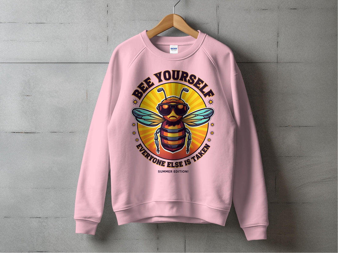 A person wears Garment Graphics blue Summer Edition Sweatshirt featuring a cool bee in sunglasses. The phrase Bee Yourself, Everyone Else is Taken pops against the snowy backdrop, highlighting its unisex sizing allure.