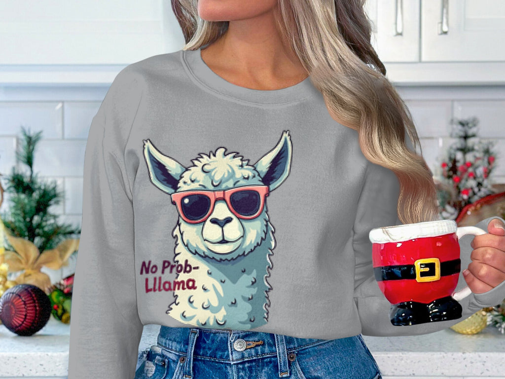 In a festive kitchen adorned with holiday decor, someone dons a Garment Graphics unisex sweatshirt featuring a llama in sunglasses and the phrase No Prob-llama, while holding a Santa-themed mug.