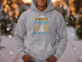 A person is wearing a Garment Graphics gray fishing hoodie with a unique design that reads, I’m not addicted to fishing, we are just in a very committed relationship. The classic fit matches the backdrop of blurred lights and softly falling snowflakes.