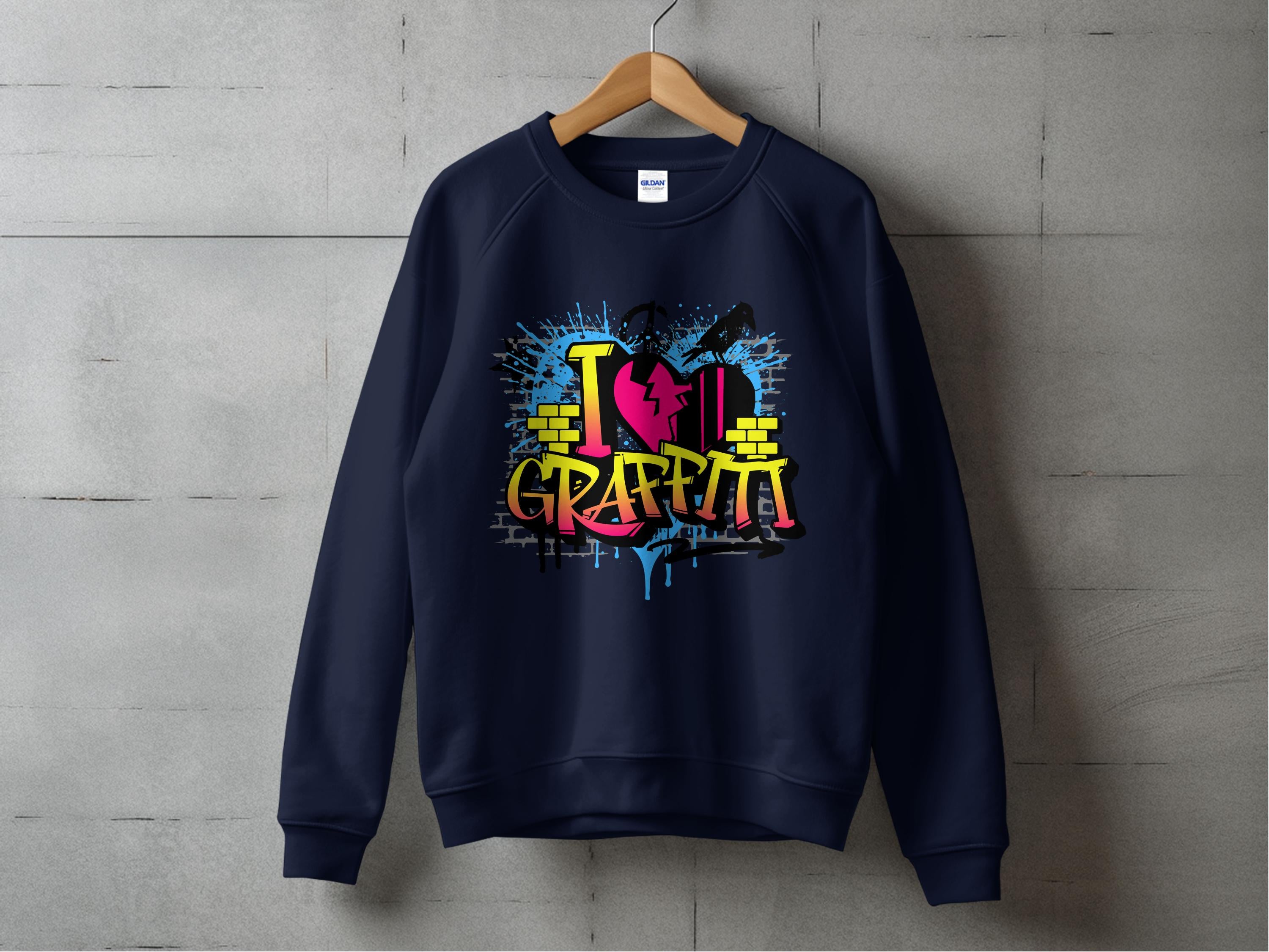 A dark blue sweatshirt by Garment Graphics is displayed on a wooden hanger against a concrete wall, featuring vibrant street art and graffiti-style text I Love Graffiti. The design includes vivid paint splatters and brick patterns for an energetic effect.