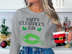 Amid festive kitchen decorations, a long-haired person holds a Santa-themed mug. They wear a gray Garment Graphics sweatshirt featuring green lips, shamrocks, and the phrase Happy St. Patricks Day, embracing the clover kiss of holiday spirit.