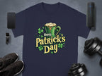 Garment Graphics navy statement St. Patricks Day t-shirt features a green mug, shamrocks, and Happy Patricks Day, artistically framed by a smartphone, watch, shoes, speaker, and dumbbells on a sleek gray background.