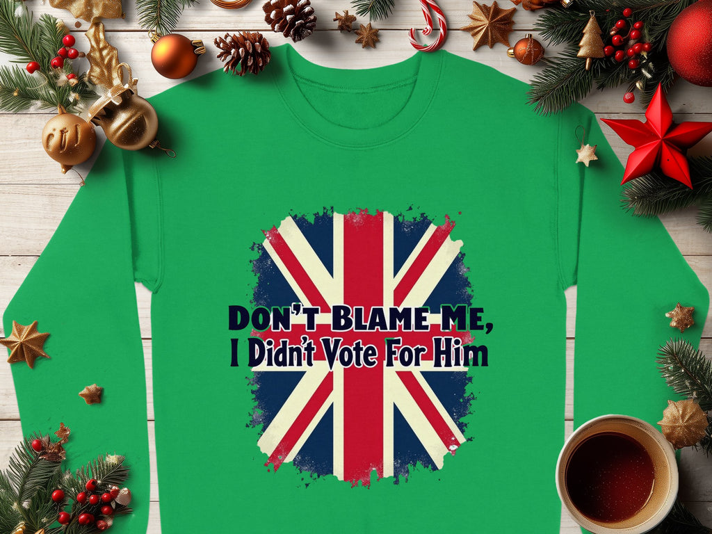 Garment Graphics offers a cozy green sweatshirt with a bold distressed Union Jack and the text Dont Blame Me, I Didnt Vote For Him, styled amidst holiday decor like ornaments, pine branches, and a warm cup of coffee.