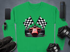 Garment Graphics vibrant sweatshirt is ideal for motorsport fans, showcasing a graphic of a red racing car with crossed black and white checkered flags. Surrounding this on the gray surface are a smartphone, wireless speaker, smartwatch, sneakers, and dumbbell set.