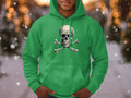 A trendsetter wears a vivid green hoodie featuring a skull and crossbones by Garment Graphics. The softly blurred background, sprinkled with glowing lights and drifting snow, creates a peaceful winter scene.