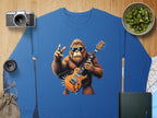 Garment Graphics blue rocking gorilla sweatshirt features a gorilla illustration with sunglasses, holding an electric guitar, and flashing a peace sign. Its surrounded by a camera, lens, kiwi slices, book, map, and pouch—ideal for music lovers.