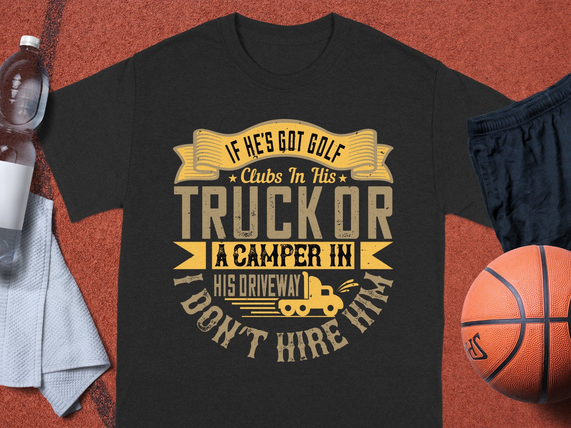 A black Garment Graphics T-shirt with the humorous quote If hes got golf clubs in his truck or a camper in his driveway, I dont hire him in yellow and gray sits on a red surface, surrounded by a basketball, water bottle, and towel—an ideal gift.