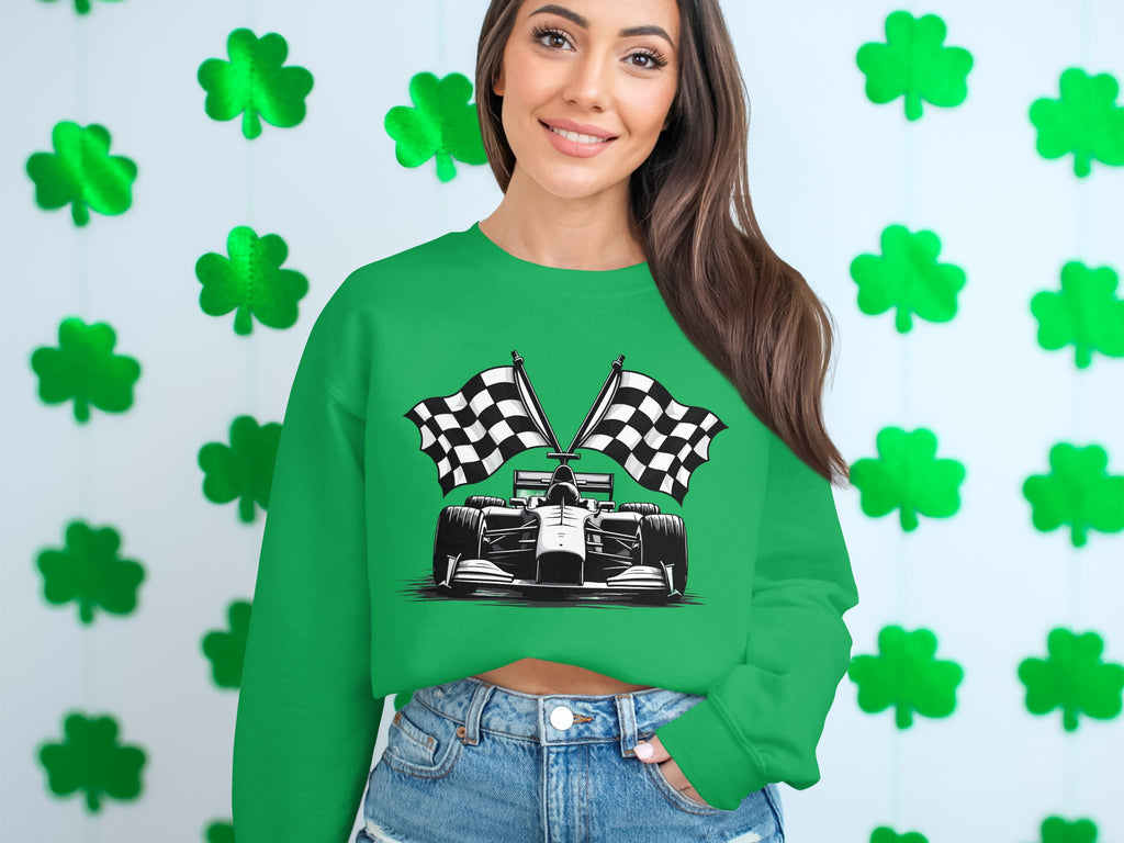 A woman stands smiling in front of a wall of green shamrocks, wearing Garment Graphics unique design—a green racing car sweatshirt with checkered flag print—and blue jeans. Her long hair cascades over one shoulder.