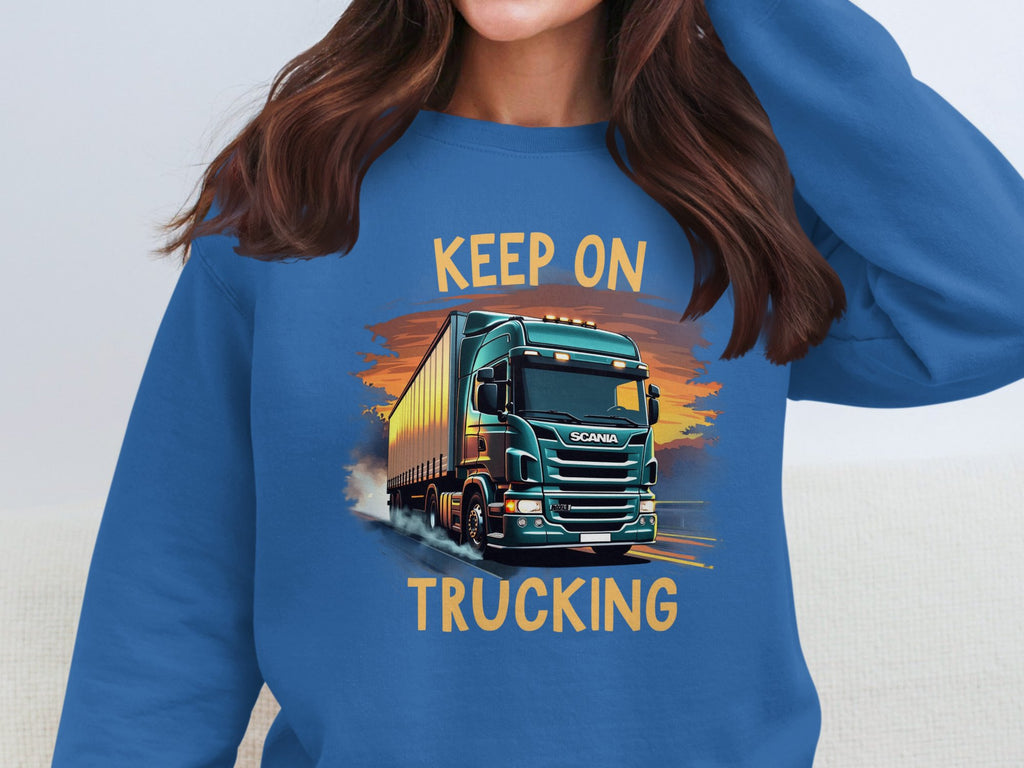 A Garment Graphics blue graphic sweatshirt features a green truck on a road, ideal for truck enthusiasts. The vibrant illustration has KEEP ON above and TRUCKING below. The persons face is hidden in the image.