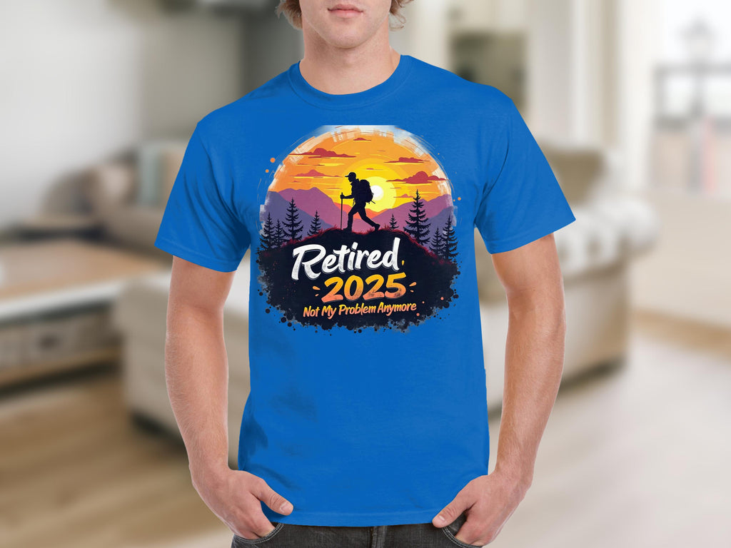A person wears a blue sunset T-shirt by Garment Graphics featuring a hiker silhouette and the bold text, Retired 2025, Not My Problem Anymore, capturing the essence of retirement. The blurred room setting adds to the relaxed vibe.