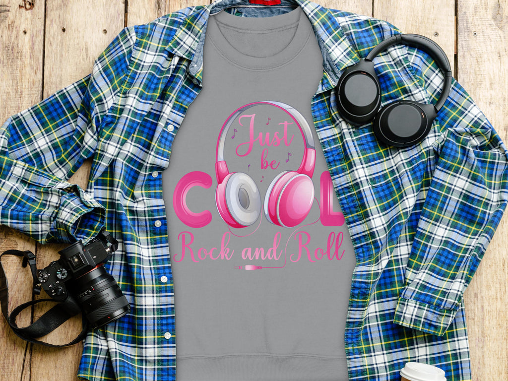 A Garment Graphics plaid shirt is open over a gray tee that says Just be Cool, Rock and Roll with pink headphones. Ideal for music and fashion fans, a black camera is on the left and Rock and Roll headphones are on the right, all set on wood.
