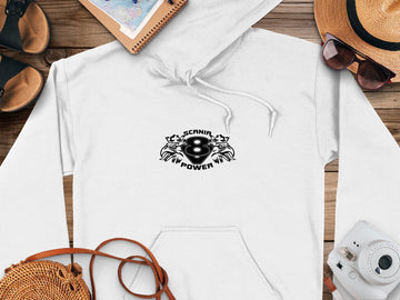 A white hoodie by Garment Graphics features a bold SCANIA V8 POWER graphic on the front and a classic fit. Its styled on a wooden surface with a notebook, straw hat, glasses, instant camera, and woven bag—perfect for Scania Power Eight Hoodies fans.