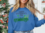 A person wears a festive Garment Graphics sweatshirt featuring a green truck and shamrocks with Happy St. Patricks Day. A subtly twinkling decorated Christmas tree stands in the background.