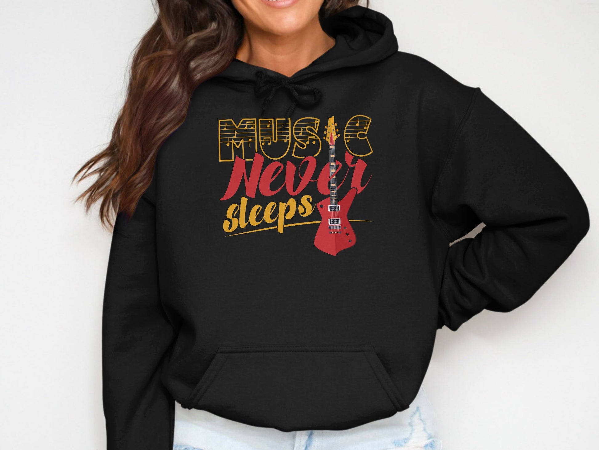 The individual is wearing a Garment Graphics classic fit black hoodie with Music Never Sleeps and a vibrant red guitar design. With long brown hair and a cheerful smile, they confidently pose with one hand on their hip.