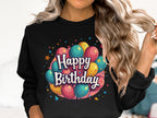 Someone with long, wavy hair sports a black Happy Birthday sweatshirt from Garment Graphics, adorned with vibrant balloon graphics. Ideal for celebrations, this unisex sweatshirt is designed to fit all sizes.