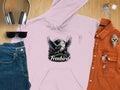 A Freebird Graphic Pullover Hoodie from Garment Graphics, featuring a bold bird with spread wings design, is laid flat. Nearby are headphones, sunglasses, a watch, keys, an orange shirt, and blue jeans. This distinctive piece seamlessly enhances any casual outfit.