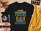 A black unisex sweatshirt by Garment Graphics features the text Im not addicted to fishing; we are just in a very committed relationship in diverse fonts and colors, surrounded by sunglasses, makeup, brushes, jewelry, a yellow blazer, and pink shoes on wood.