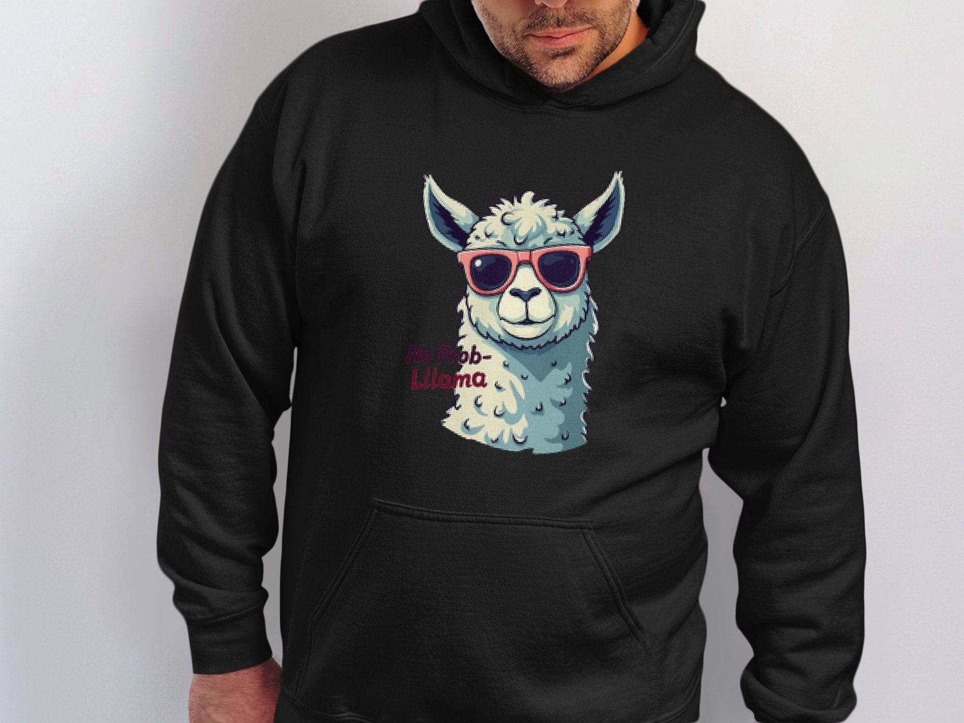 A person wears a Garment Graphics classic fit black llama hoodie with a llama in funny sunglasses and the text No Prob-llama, gazing slightly downward against a white background.