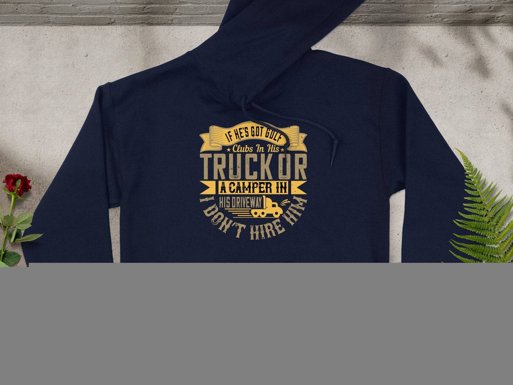 Garment Graphics navy golf hoodie with funny quote: If hes got cut-off clubs in his truck or a camper in his driveway, I dont hire him. An ideal gift displayed flat next to green and yellow leaves on light gray.
