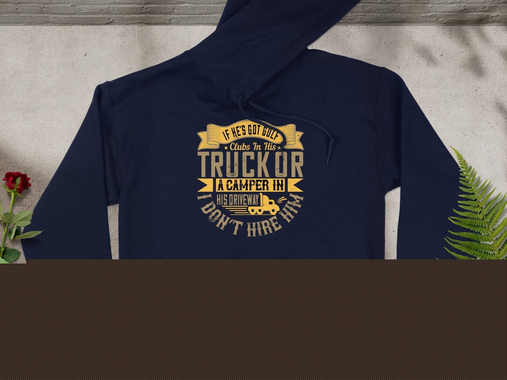 Garment Graphics navy golf hoodie with funny quote: If hes got cut-off clubs in his truck or a camper in his driveway, I dont hire him. An ideal gift displayed flat next to green and yellow leaves on light gray.