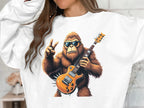 A person wears a white Garment Graphics music lovers sweatshirt showcasing a vibrant, cartoon-like illustration of Bigfoot holding an electric guitar, wearing sunglasses, and making a peace sign. Its perfect for those who enjoy fun and music vibes.