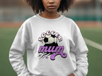 A person on a sports field wears a white Garment Graphics sweatshirt with a vintage Soccer Mum design, showcasing a soccer ball and purple stars.