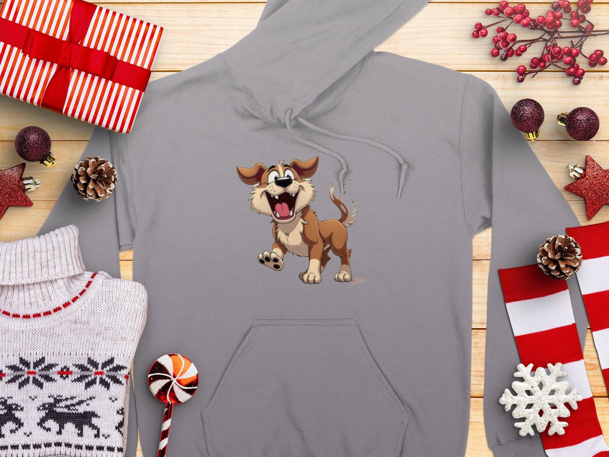 Garment Graphics presents a gray cartoon puppy hoodie surrounded by festive items: gifts, ornaments, pine cones, a striped lollipop, snowflake decoration, and reindeer sweater—all on wood—perfect for dog lovers seeking a playful wardrobe addition.